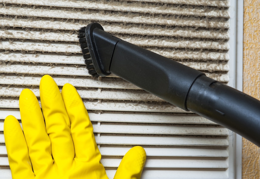 Hand in yellow glove and vacuum cleaner pipe on vent