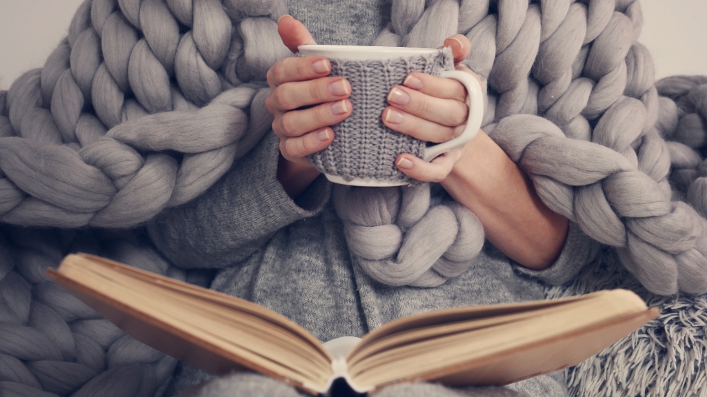 Cozy Woman covered with warm soft merino wool blanket reading a book. Relax, comfort lifestyle.